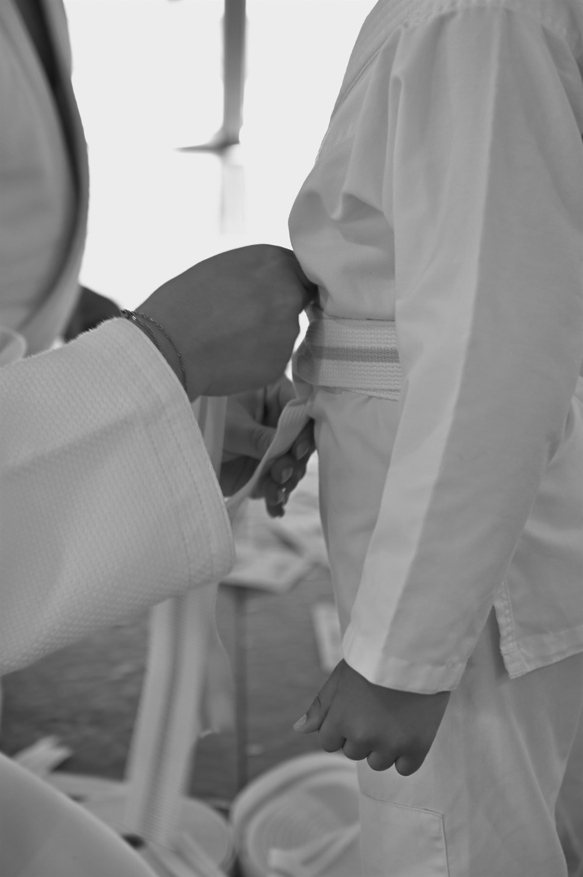 Un adulte ajuste la ceinture de judo d'un enfant, noir et blanc